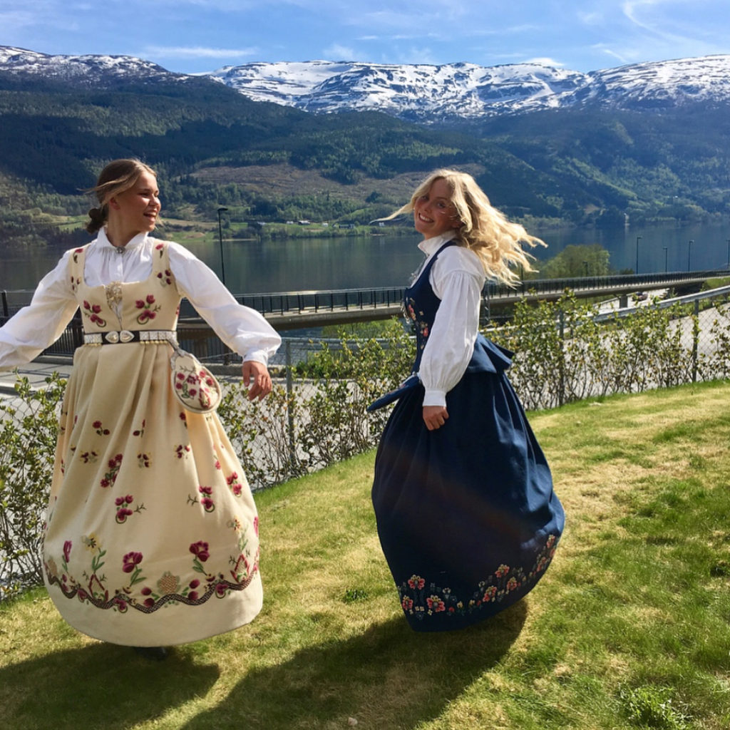 To vakre unge damer i bunad danser for fjellene og hverandre ved Voss folkehøskule