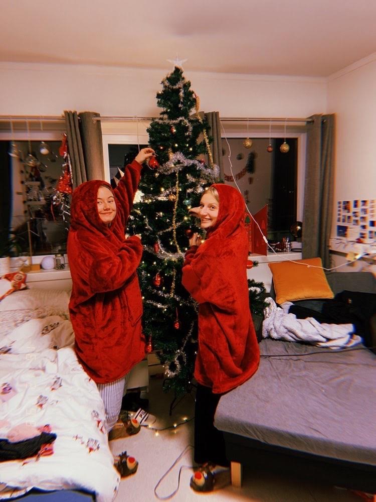 To jenter i røde gensere pynter et juletre på rommet sitt.