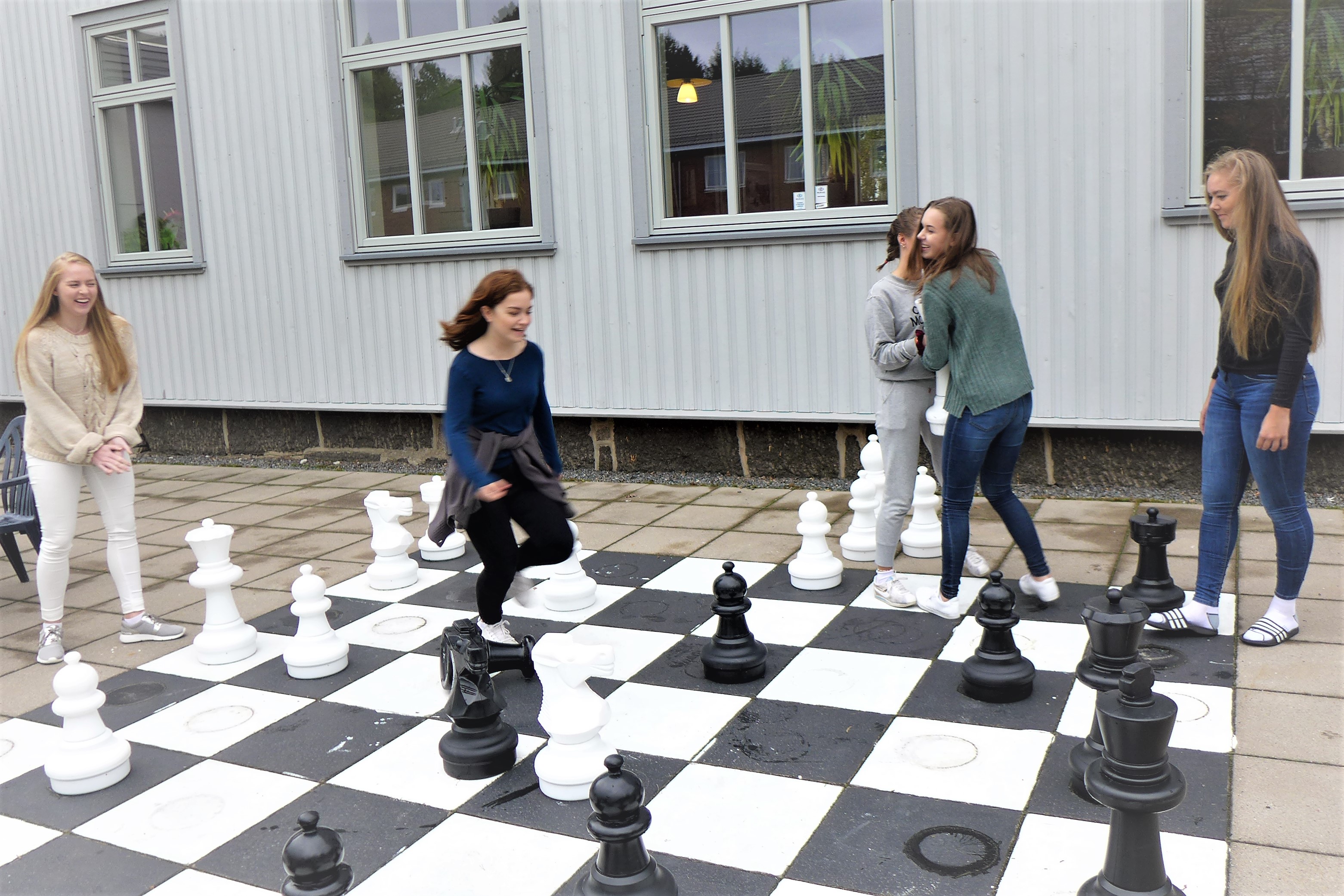 Fem jenter spiller sjakk med store brikker ute