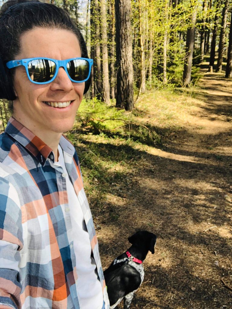 Mann går på tur i skogen med headset og hund.