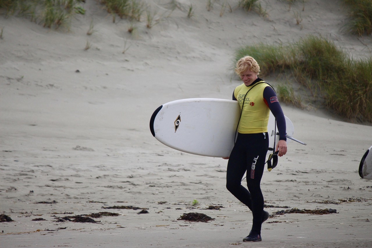 Sander med surfebrett under armen, på stranda
