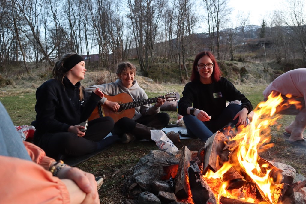 tre medelever rundt bålet, en har gitar