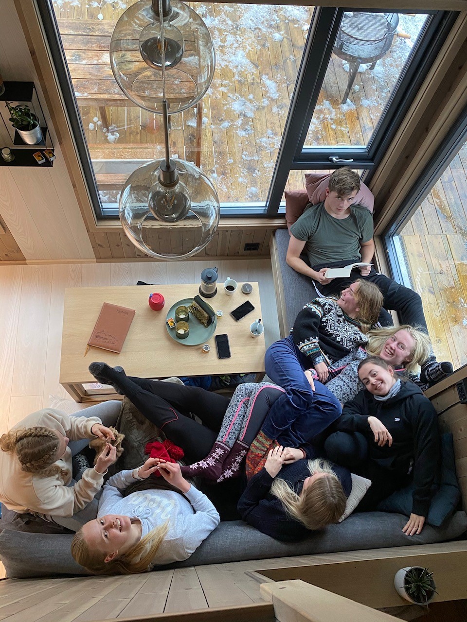 På hyttetur. Bilde tatt ovenfra av sju elever som sitter tett sammen i samme sofa.