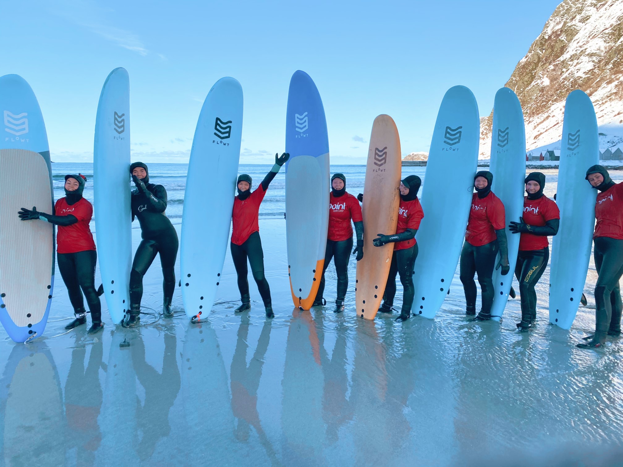 åtte elever med hvert sitt surfebrett oppstilt på stranda