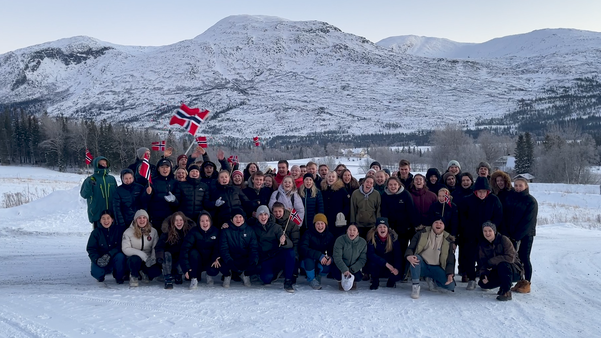 En klasse står samlet, smiler og vinker med flagg for å gratulerte med dagen.