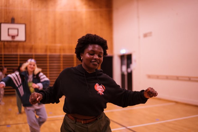 Trixie danser, i gymsalen. Flere medelever i bakgrunnen.