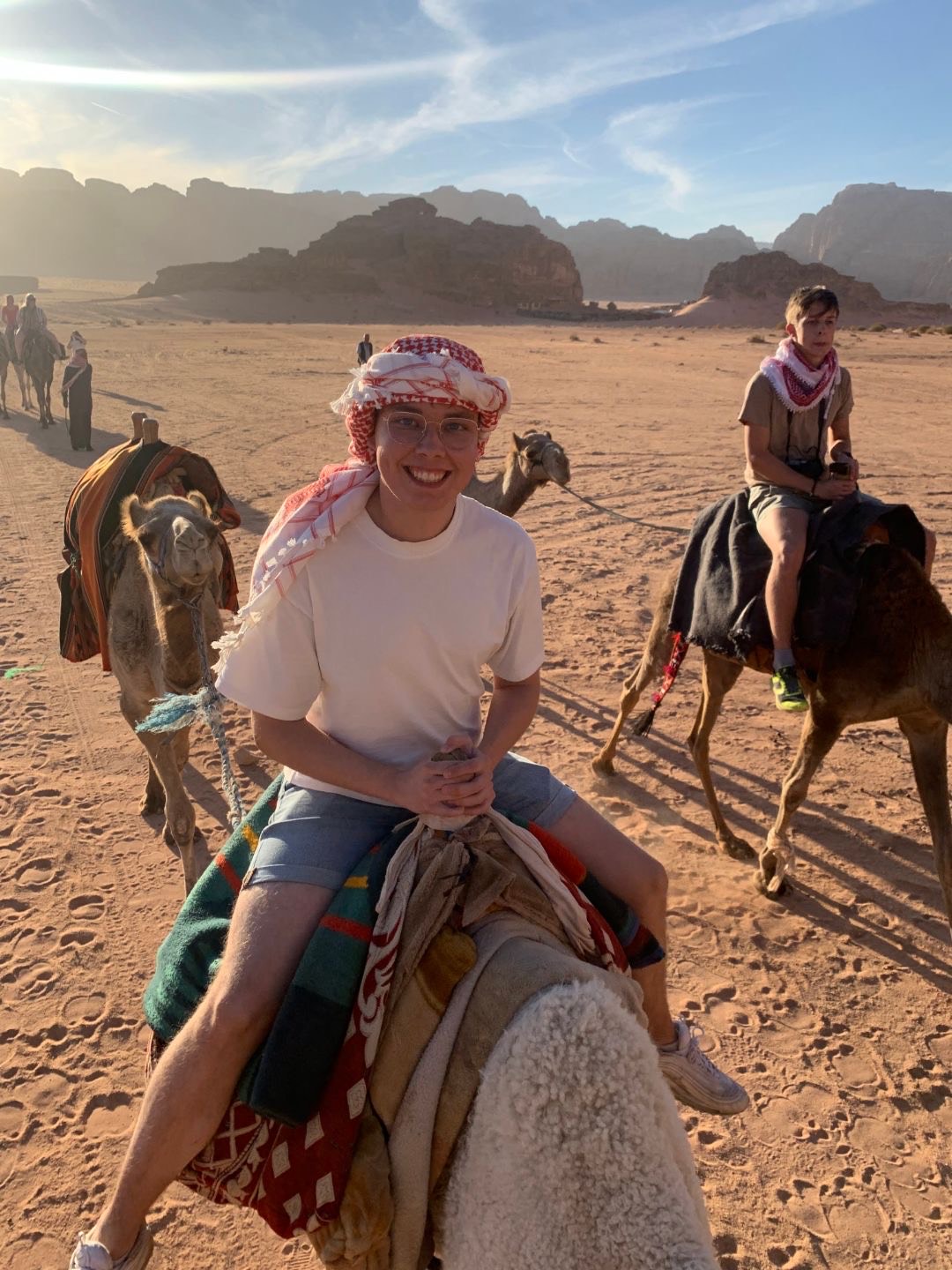 Alexander rir på en kamel, smiler. Flere elever på kameler i bakgrunnen.