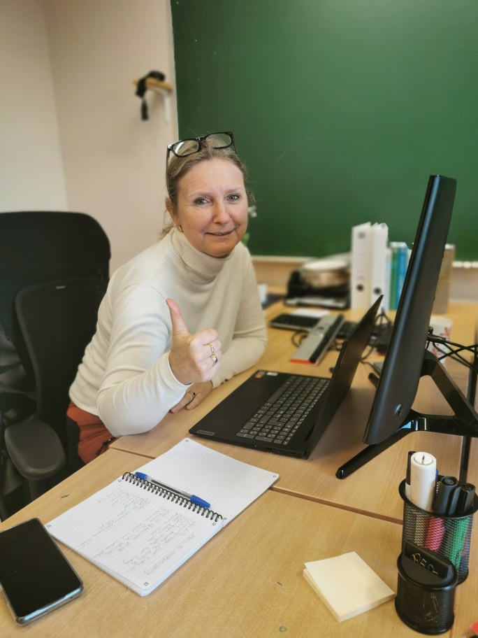 Kvinne sitter foran en PC ved en kontorpult med tommelen opp.