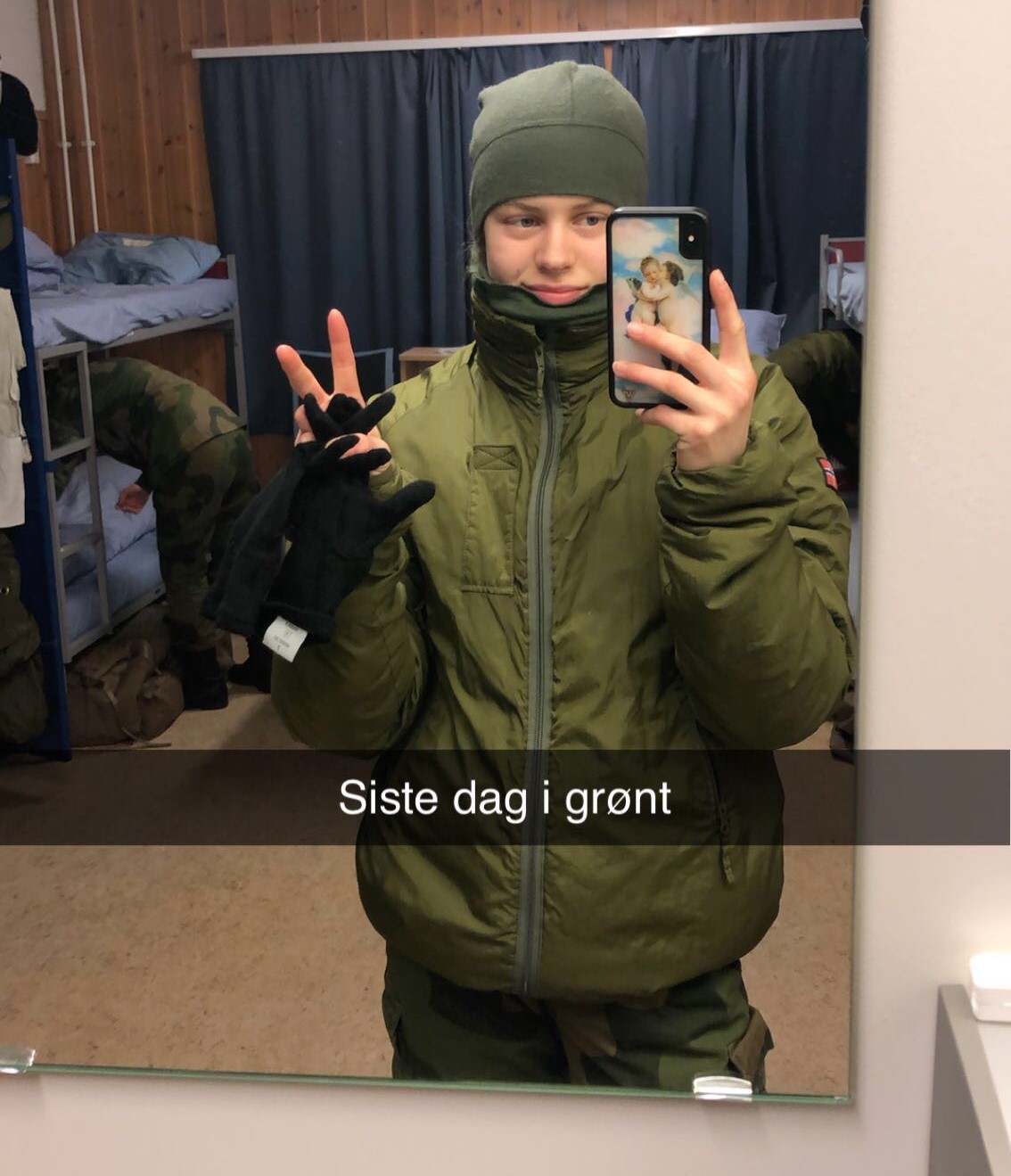 Speilselfie av en kvinnelig soldat som viser peacetegn. På bildet står det