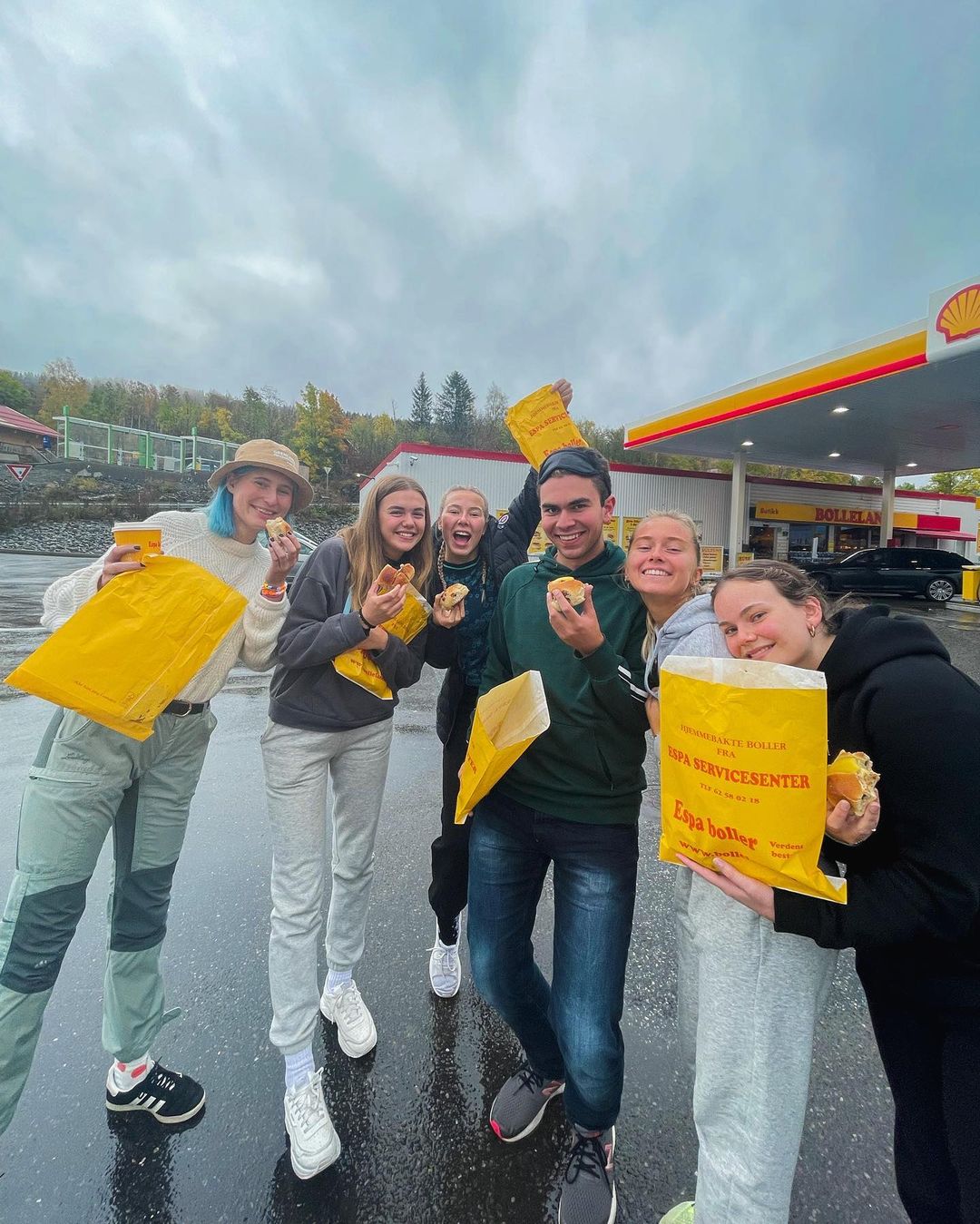 En gjeng med elever står utenfor en bensinstasjon med papirposer i hendene.