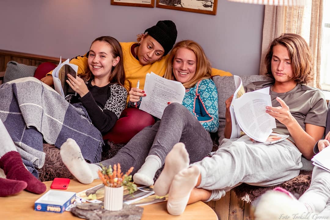 En gjeng elever sitter i en sofa i kosebukser med pledd rundt seg.