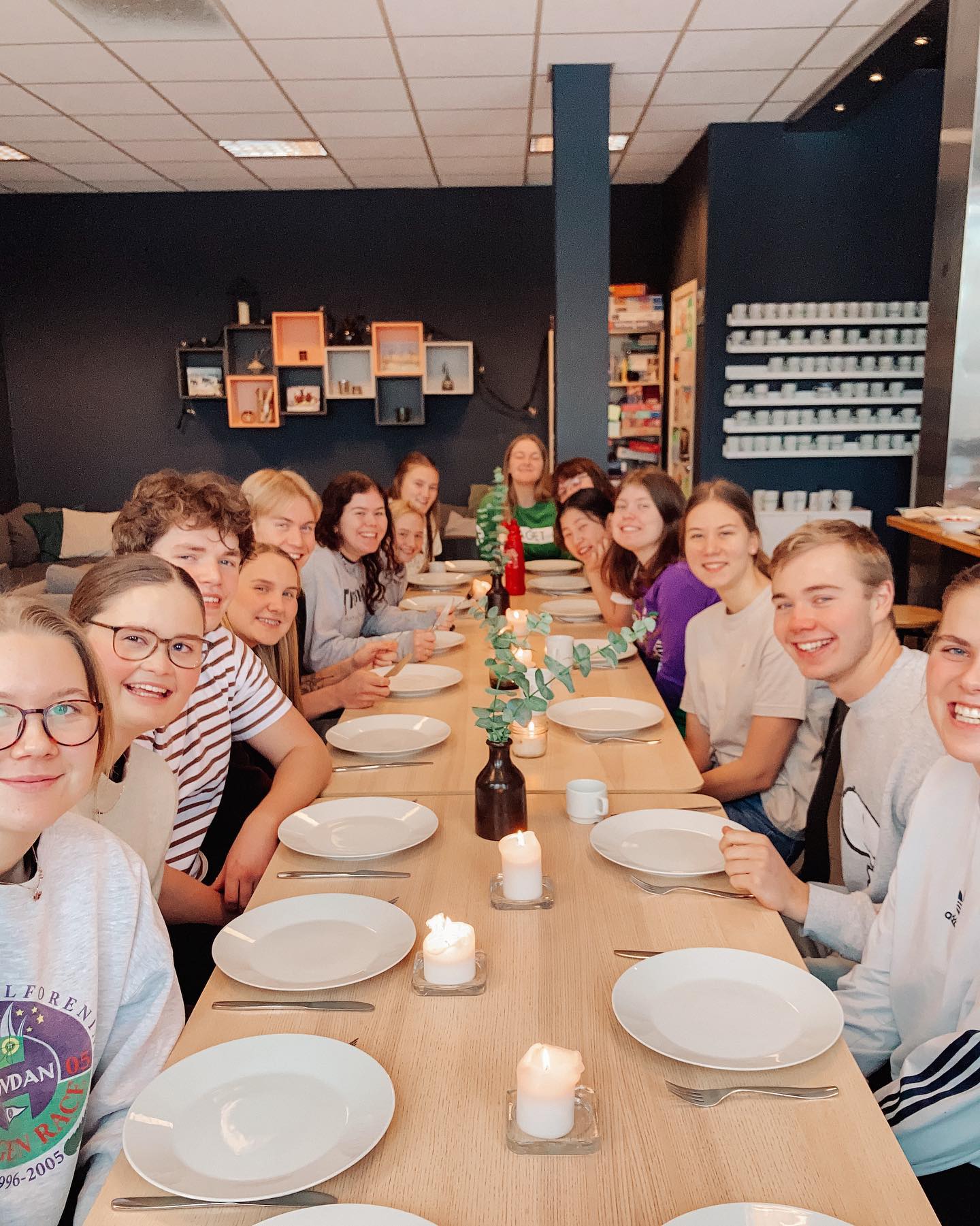 En stor gruppe elever sitter rundt et bord med tallerkner på bordet