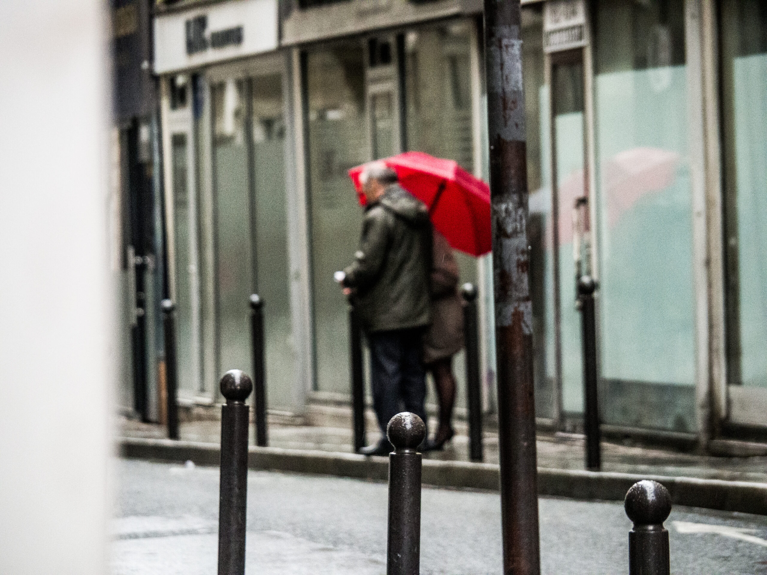 En mann på gata med rød paraply i regnvær sett bakfra