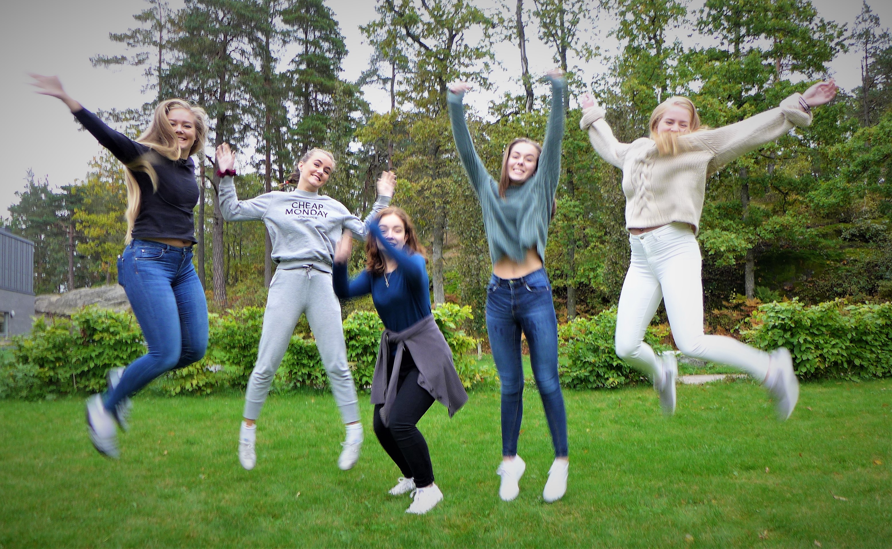 Fem jenter hopper på en plen