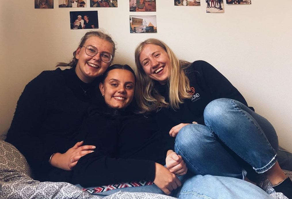 Tre jenter sitter på ei seng på et folkehøgskolerom.
