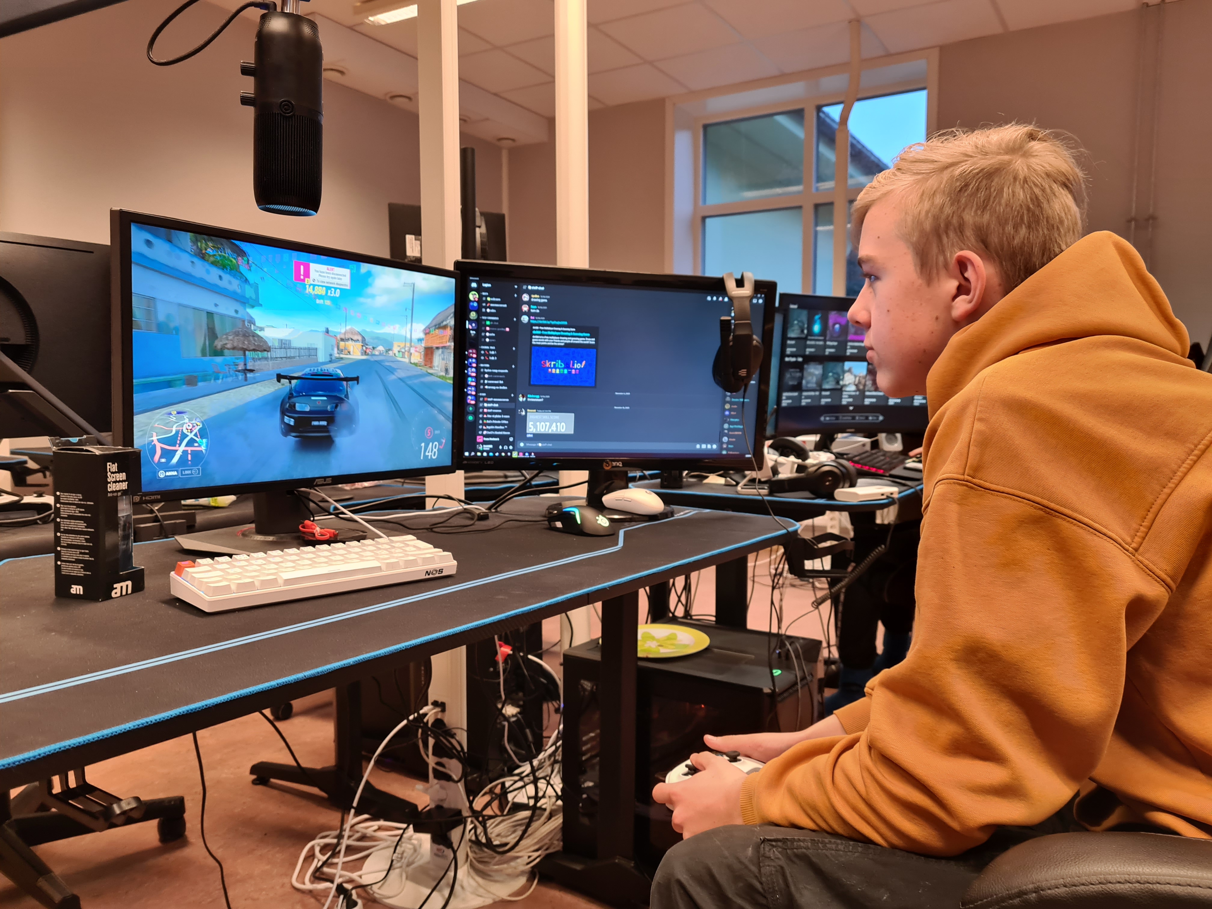 Vetle Øverland foran flere pc-skjermer, med spillkonsollen i hendene
