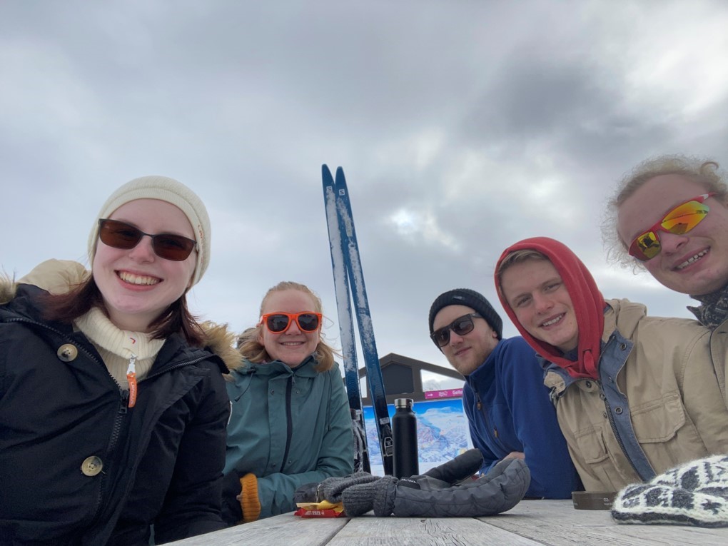 pause på skitur. Fem elever med solbriller rundt et bord, ski i bakgrunnen.