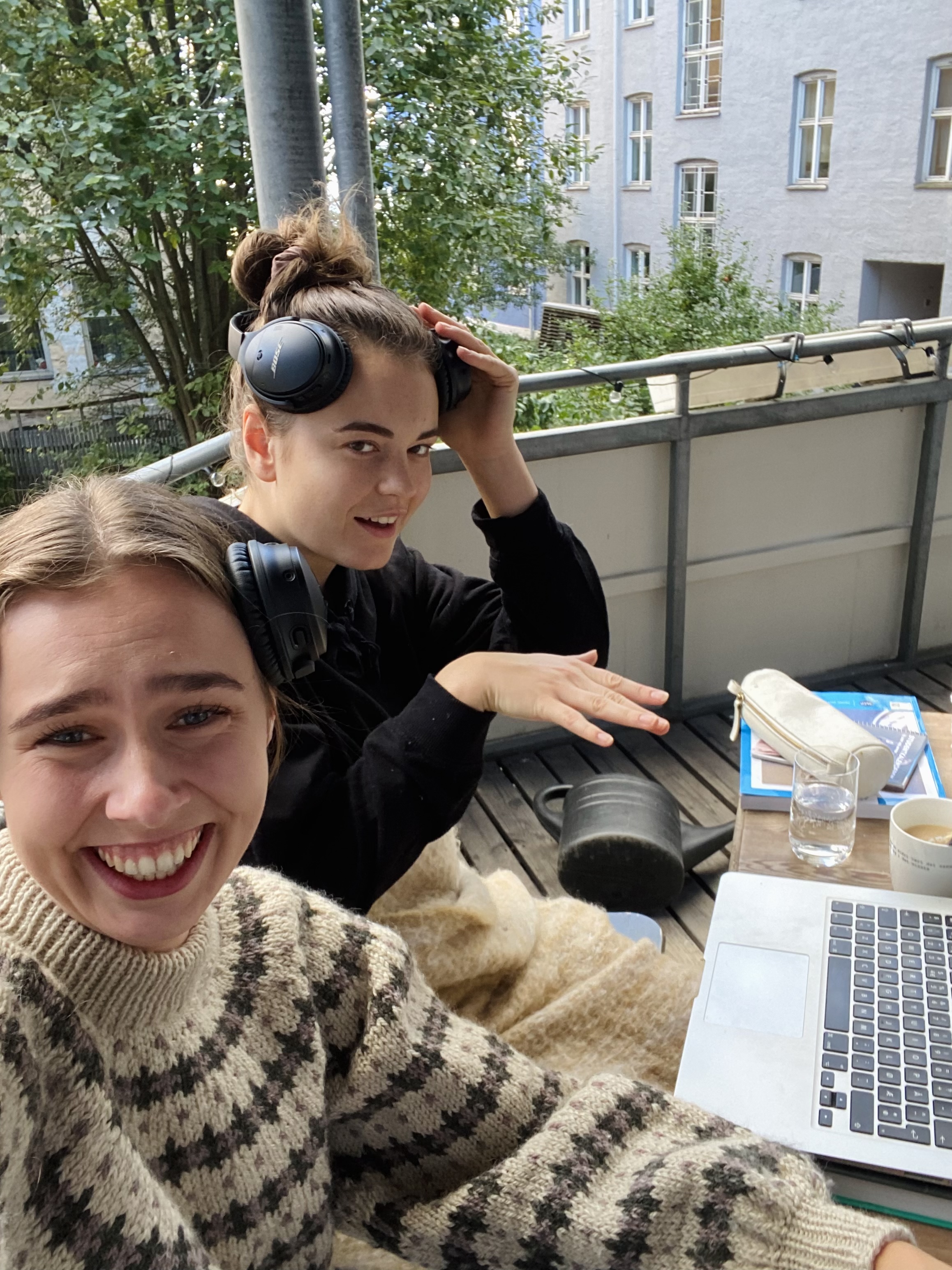 To kvinnelige studenter sitter på en veranda med datamaskinene sine og studerer. De smiler og mot kamera.
