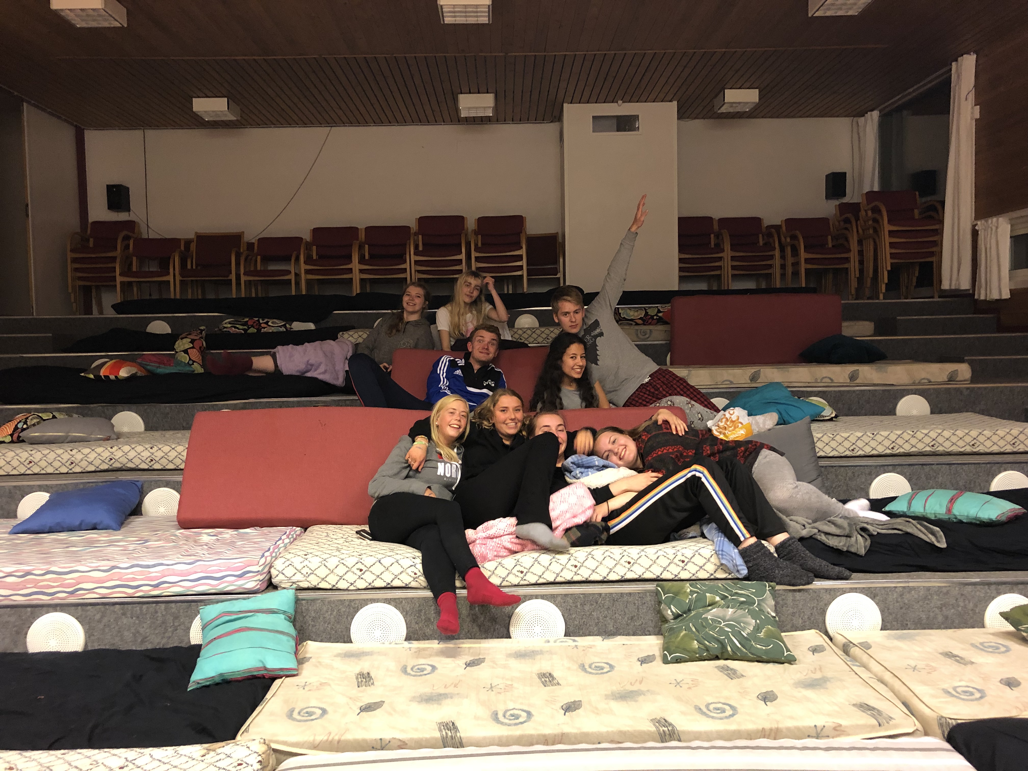 En gruppe elever sitter på madrasser i en stor sal på en skole.
