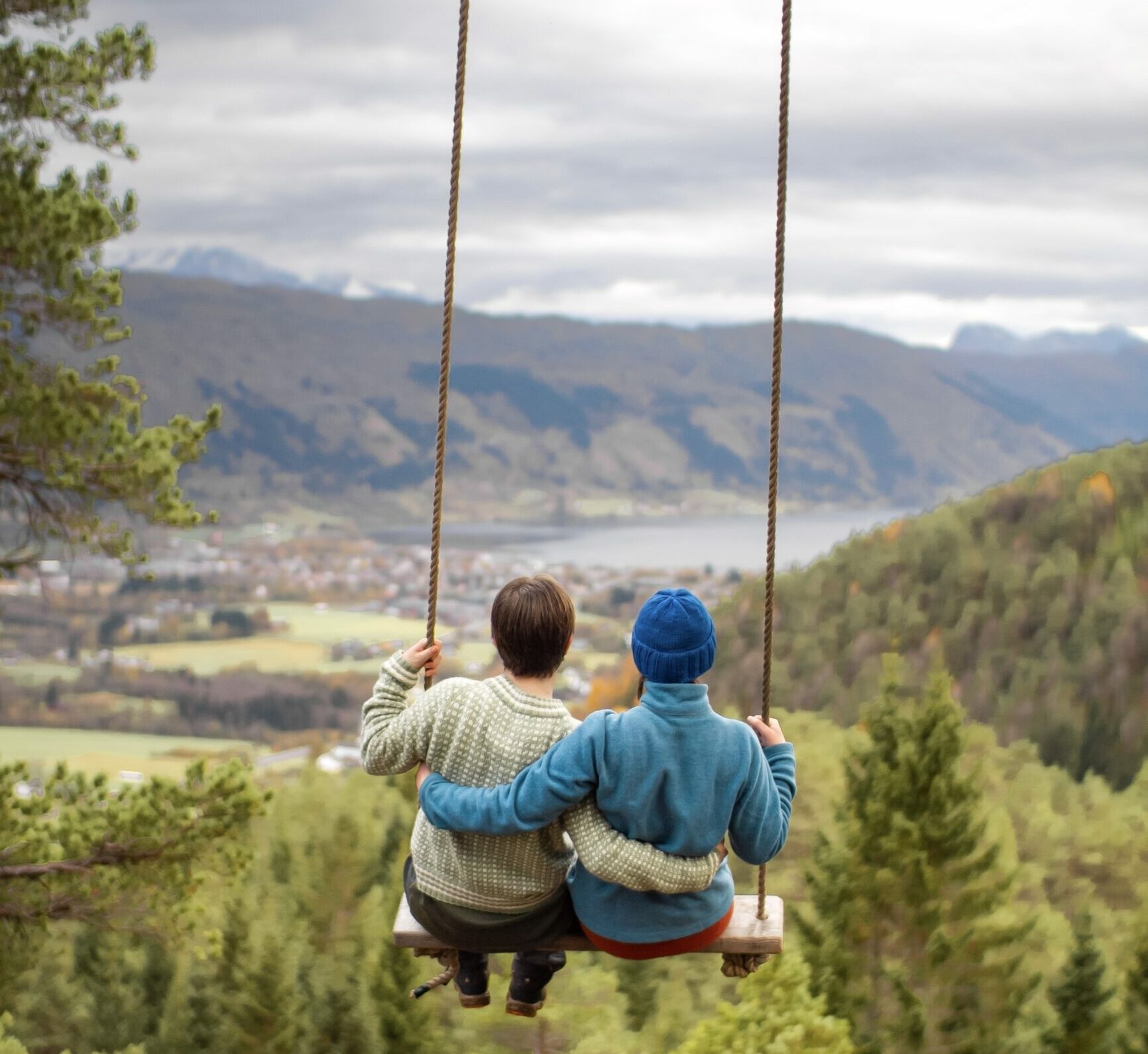 To personer på en huske med utsikt ut over en dal og en fjord