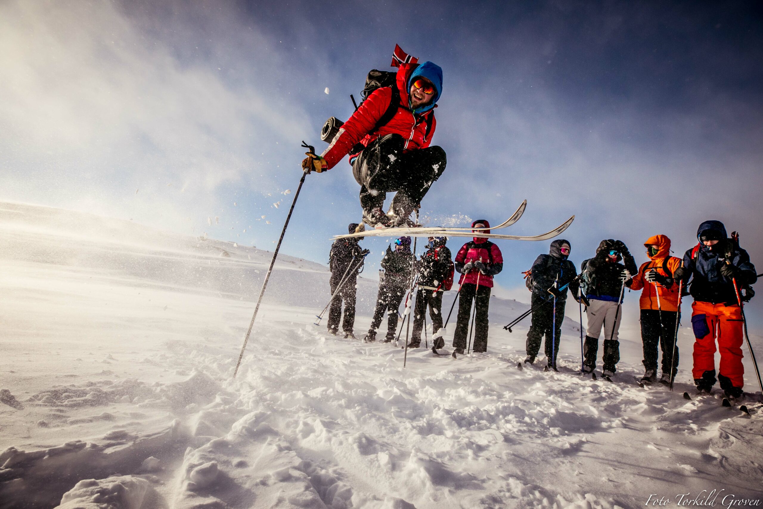 En person hopper på ski, mens andre står å ser på. 