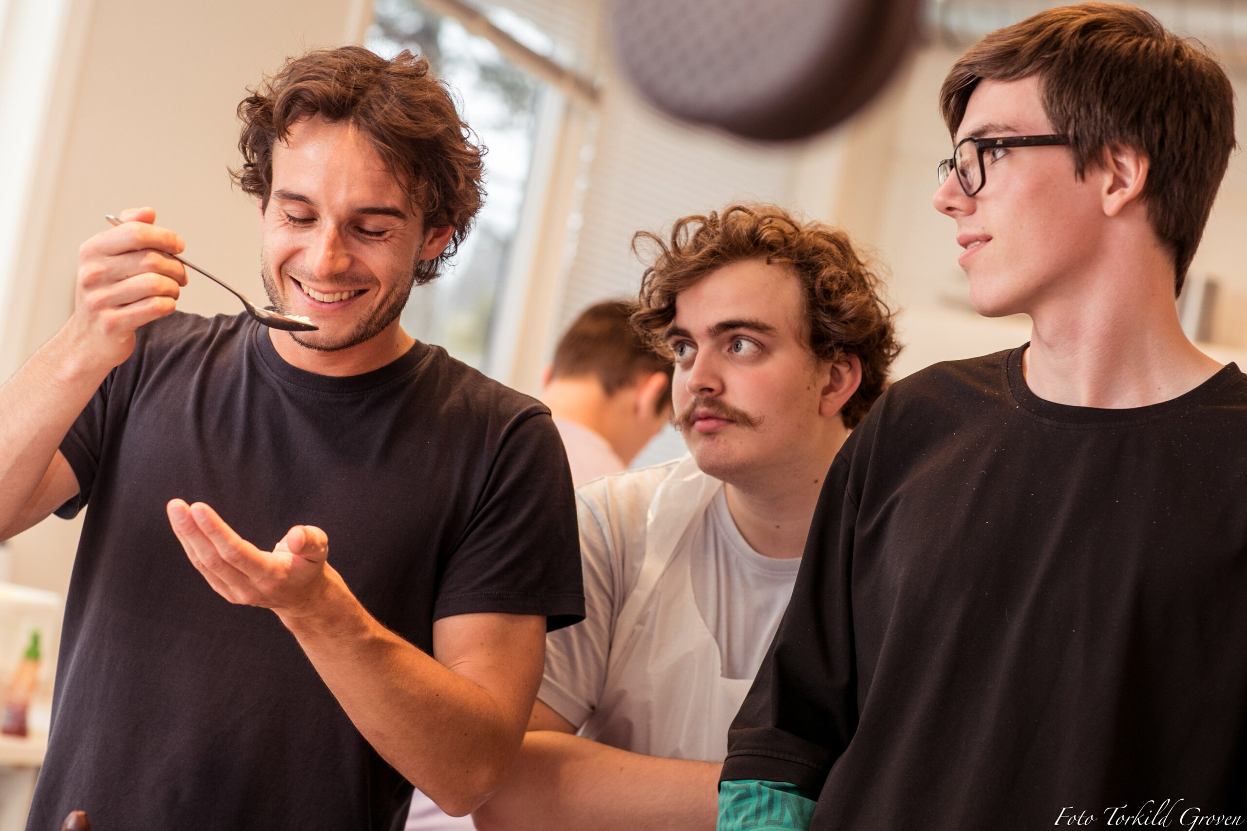 To personer ser på en tredje som har en skje på vei til munnen