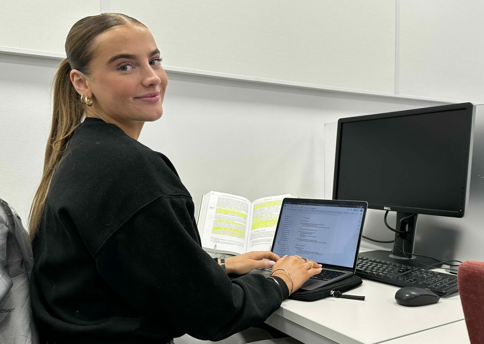 en ung kvinne som sitter på en pult med skolebøker og en pc foran se, hun snur seg og ser mot kamera