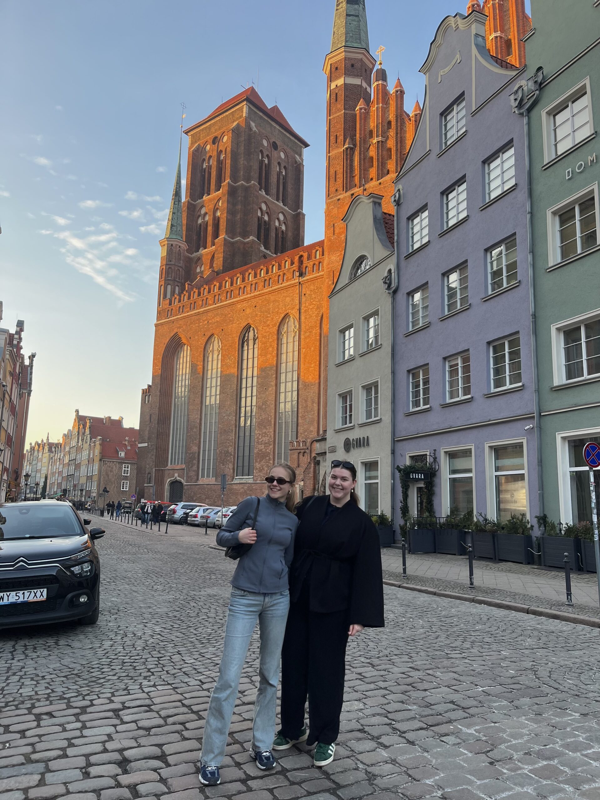 To unge kvinner som står foran historiske bygninger i en storby 