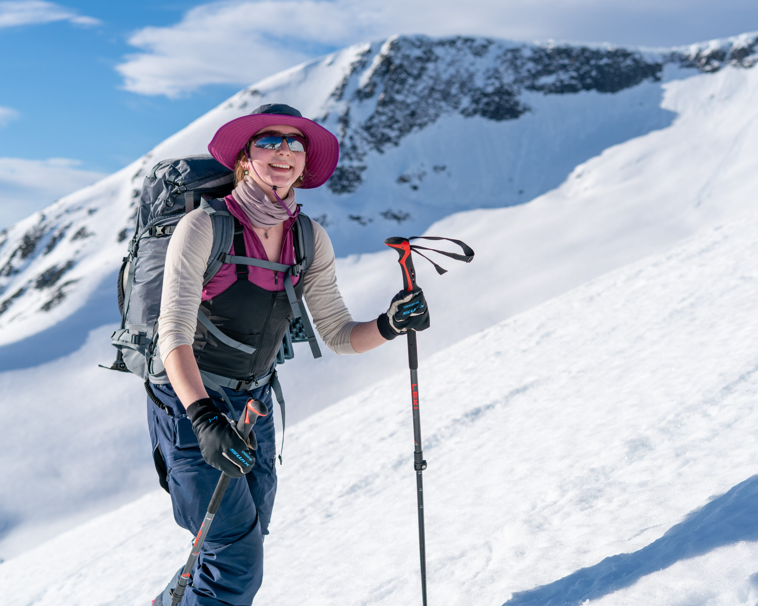 Kvinne på ski smiler til kamera. Fjell og snø i bakgrunnen