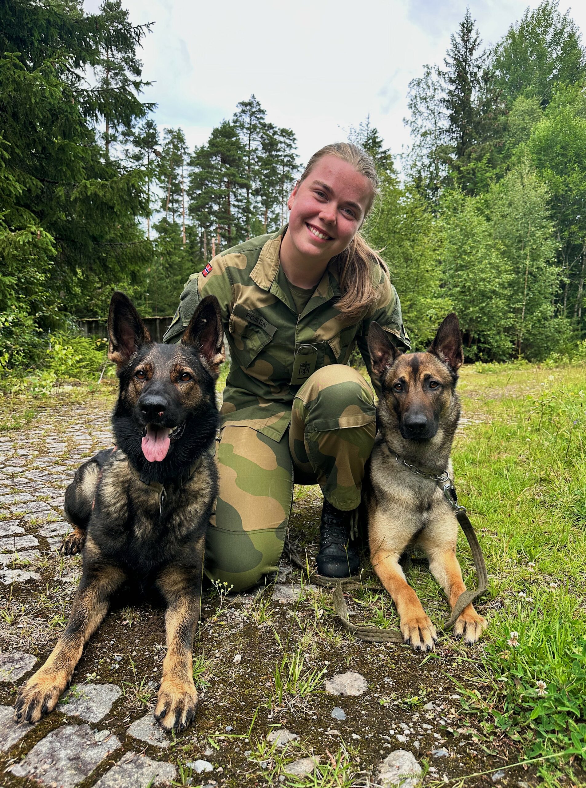 En jente i militærdress sitter med to hunder