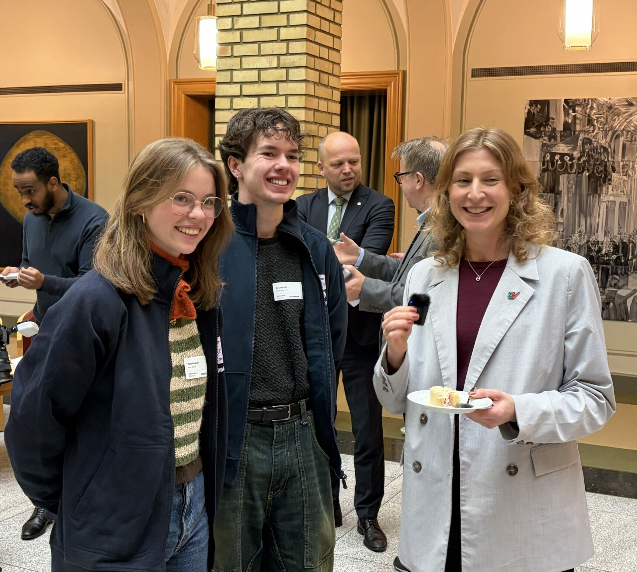 To ungdommer og en dame smiler i kamera mens de spiser kake