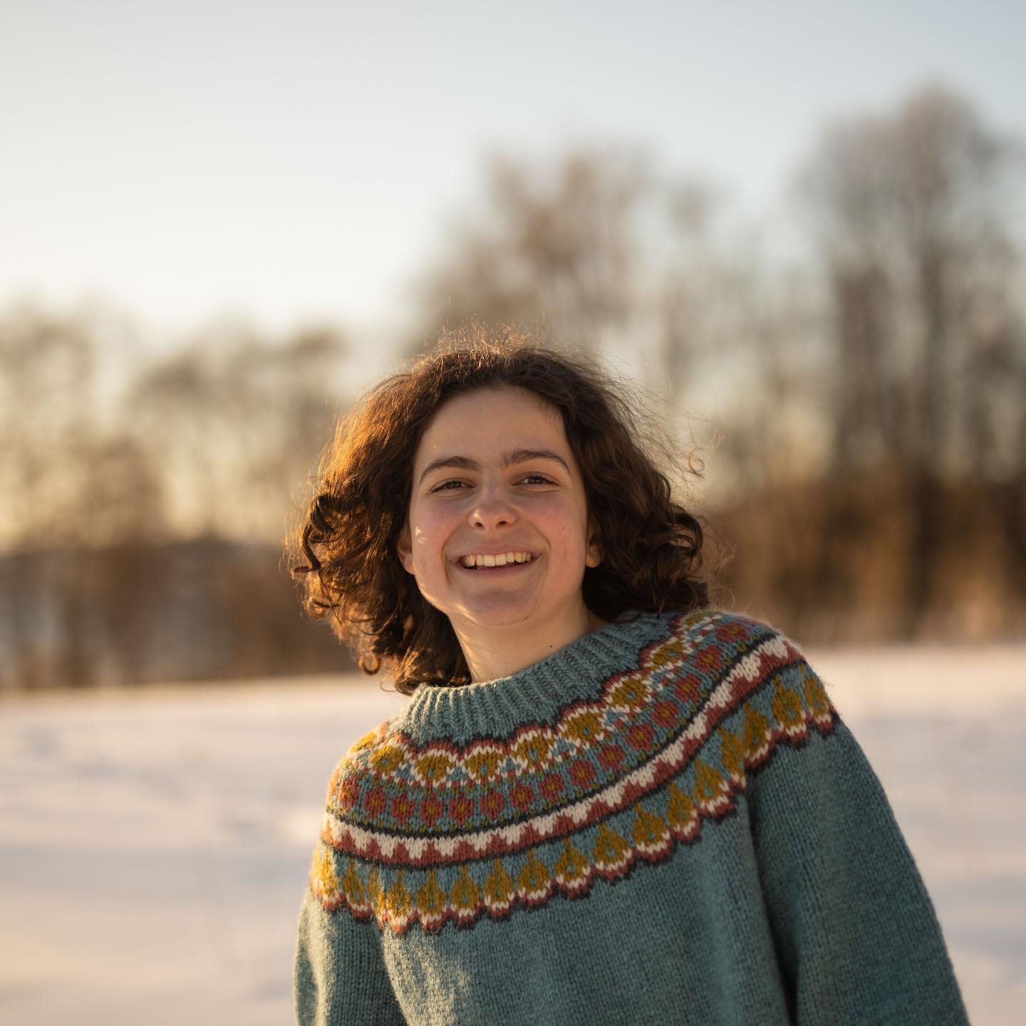 Jente med brunt hår og grønn strikkegenser i vinterlandskap.