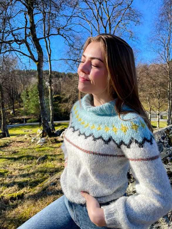 Jente med brunt hår og lys strikkegenser, sollys i ansiktet.