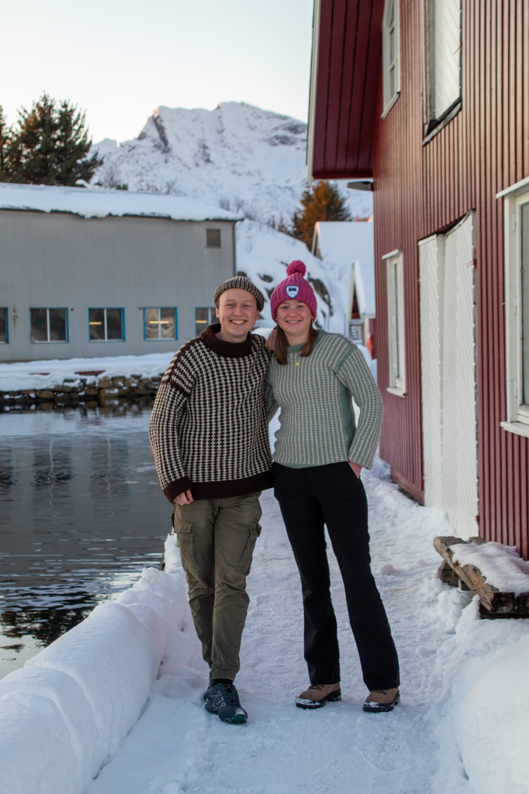 Gutt og jente i strikkegenser i vinterlandskap på kanten av en kai. 