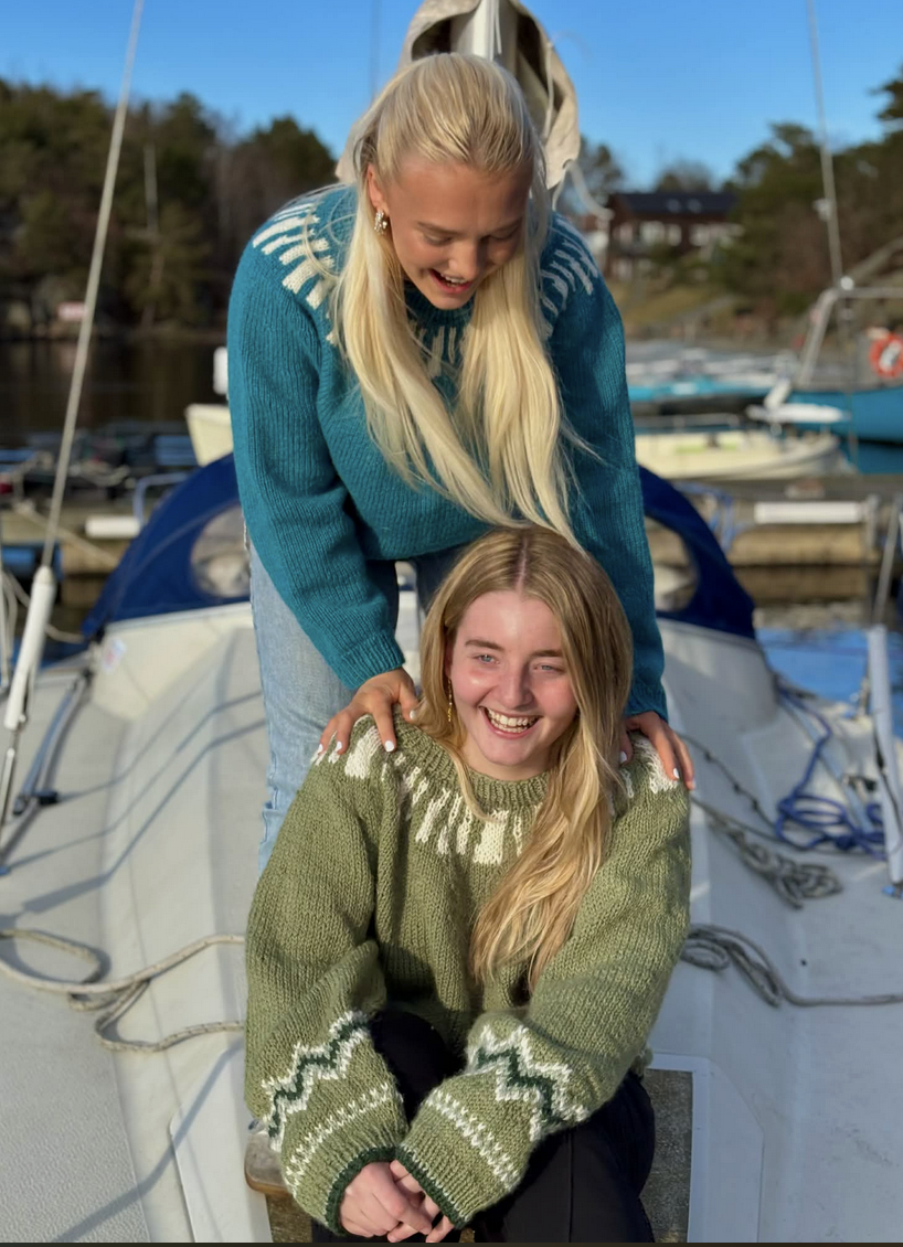 To jenter med langt hår og strikkegenser, på en båt.