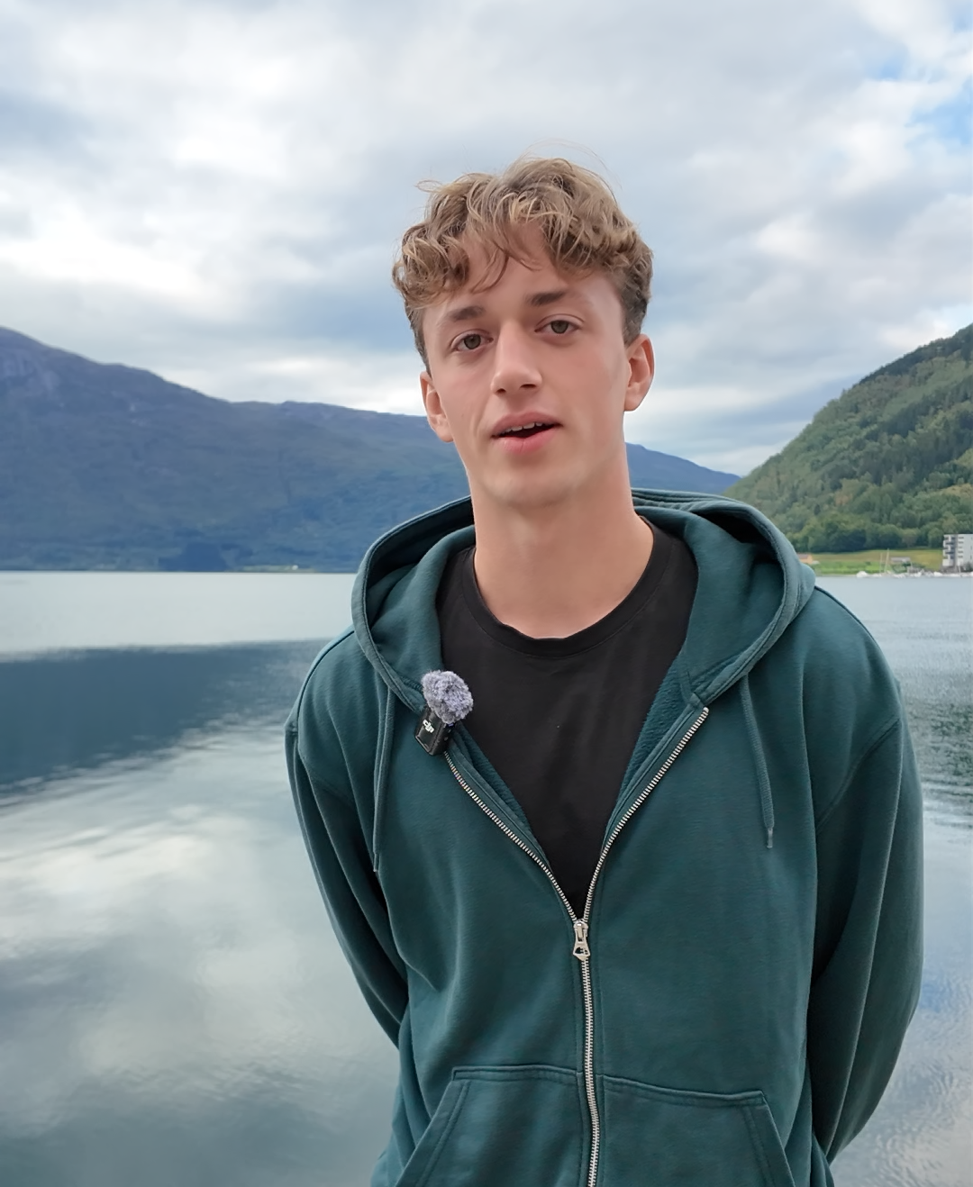 Gutt foran fjord i blågrønn hettejakke. Ulik alder.